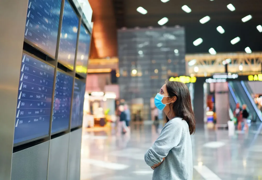 Woman in face mask looking at information board checking her flight in international airport